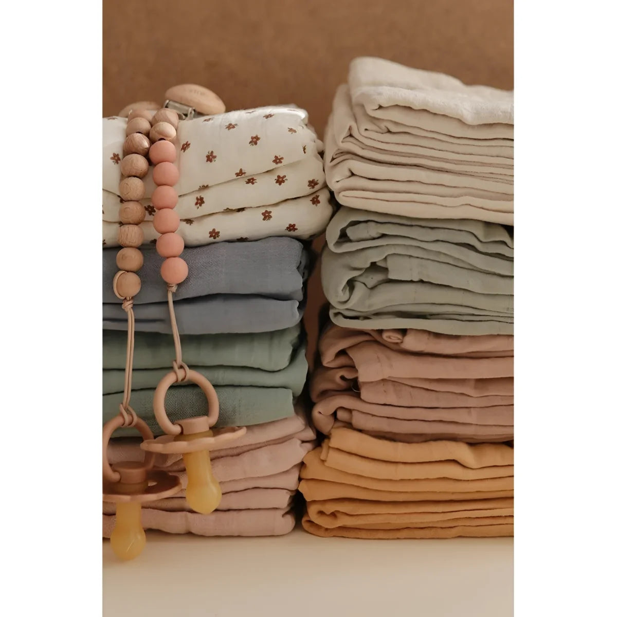 Gestapelte, gefaltete Babybekleidung und Accessoires in sanften Erdtönen