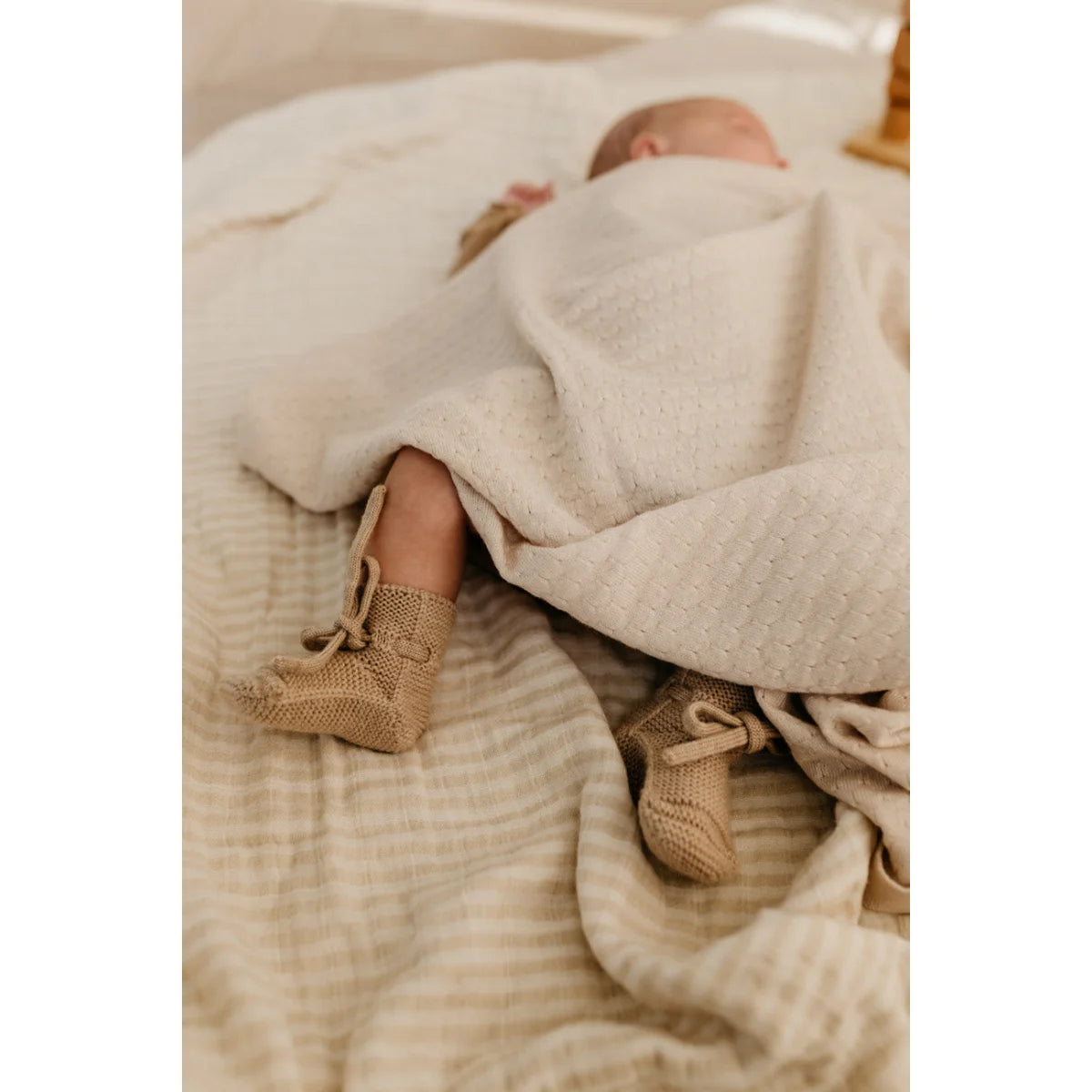 Neugeborenes Baby in weißer Decke mit gestrickten beigen Stiefeln