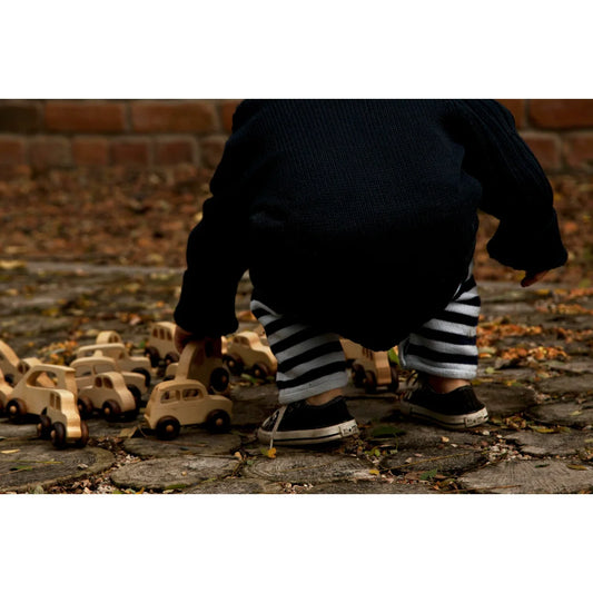 Ein kind in dunkel sweater und gestreifter hose spielt mit hölzernen bus spielzeugautos auf steinweg nachhaltige babykleidung