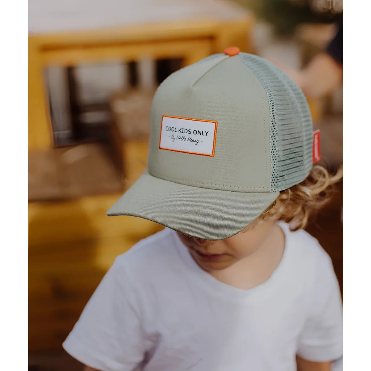 Ein hellgrünes trucker cap mini olive mit mesh-rückseite, orange knopfen und weißem label cool kids only von hello honey