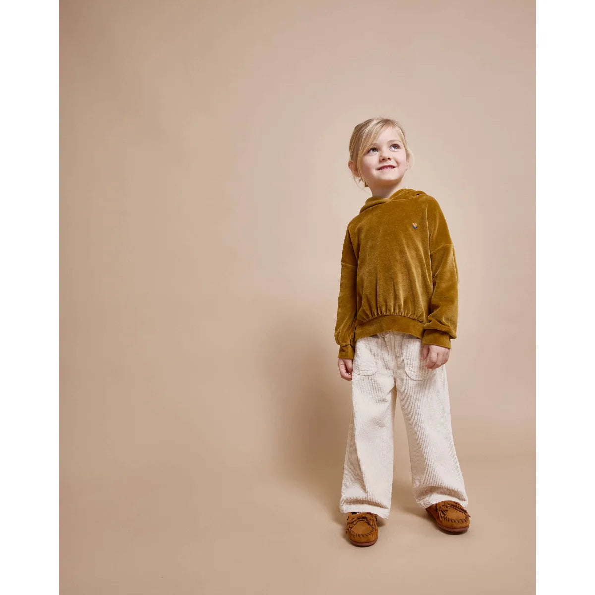 Kind eines Kindes in goldenem Samt-Hoodie und weißen Hosen in Produkt namens Corduroy Girly Pants Ivory
