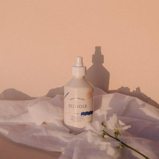 Ein weißes sleekes sprayfläschchen mit minimalistischem label von munos paris und abstrakten blauen und orangen akzenten