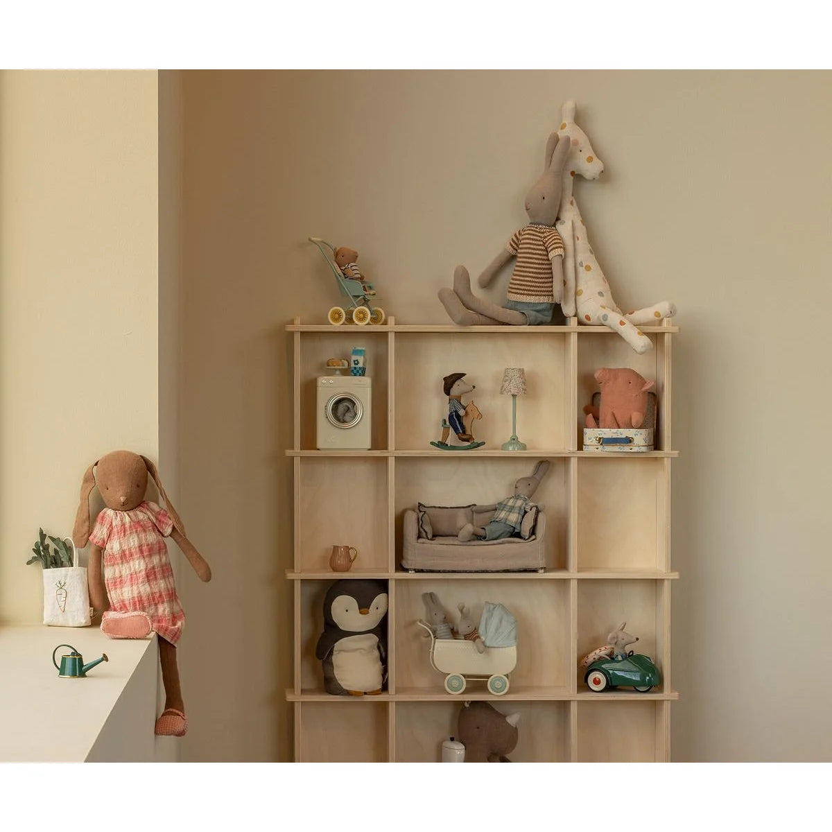 Beiges hölzernes regal mit neun fächern gefüllt mit spielzeug und gestricktem shirt und hose größe 3 nachhaltige babykleidung