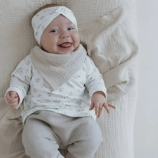 Lächelndes Baby in weißem Outfit und Haarband mit Blättern