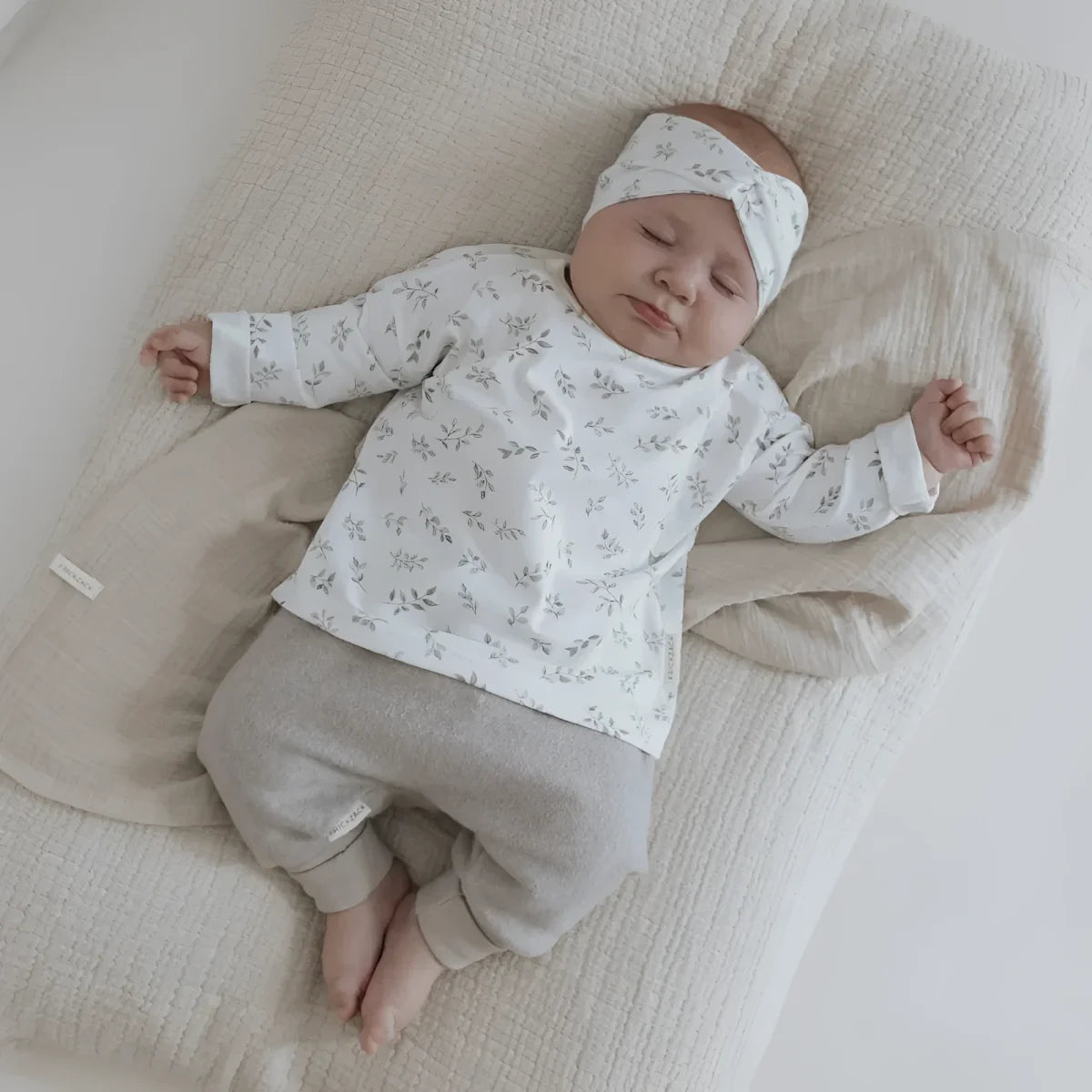 Neugeborenes Baby schläft in einem gestreiften Oberteil mit Haarband ’Blätter’