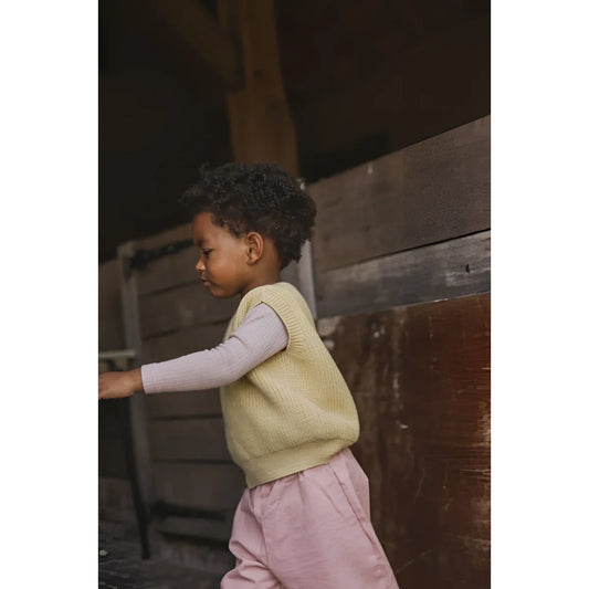 Junge trägt hellgelben Kids Vest Harvey, lila Langarmshirt und rosa Hosen