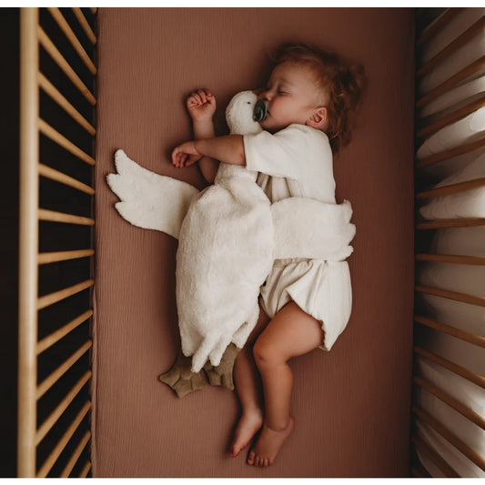 Schlafendes Baby in einem weißen Engelkostüm in einem Kinderbett mit Kuscheltier Gans