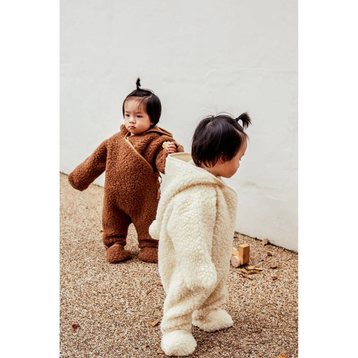 Zwei Kleinkinder in flauschigen Onesies, einer braun und einer weiß, Merino Snugglesuit Bruno