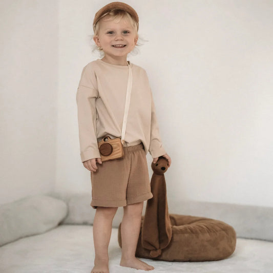 Lächelndes Kind in neutralfarbener Kleidung mit einem Stofftier in der Hand