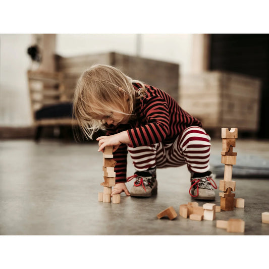 Ein kind in rot-weiß gestreifter nachhaltige babykleidung schweiz baut einen turm mit ökologischem spielzeug naturelle