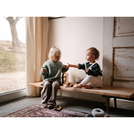 Zwei kleinkinder auf einer bank spielen mit natürlichem stapelspielzeug aus ökologischen baby- & kinderprodukten