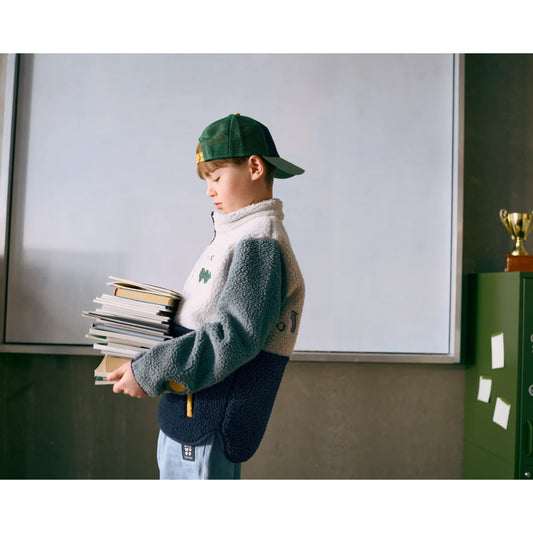 Ein kind trägt die nolan fleecejacke play mix in drei farben mit grünem baseballcap aus weichem fleece