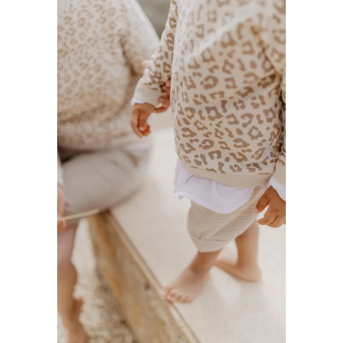 Ein kind trägt einen oversize pullover aus cremefarbenem strick mit braunem leopardenmuster nachhaltige babykleidung schweiz
