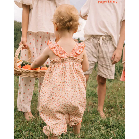 Kind in pfirsichfarbenem Blumen-Romper Picnic Jumpsuit Coral, nachhaltige Babykleidung Schweiz