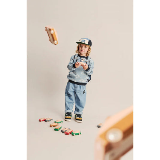 Ein kind in hellblauem sweatshirt und jeans hält holzspielzeugautos aus der rory cap cars multi mix kollektion