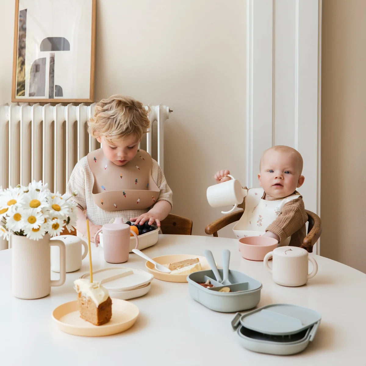 Zwei Kinder sitzen am Tisch mit verschiedenen Gerichten und Schnabelbecher in Elfenbein
