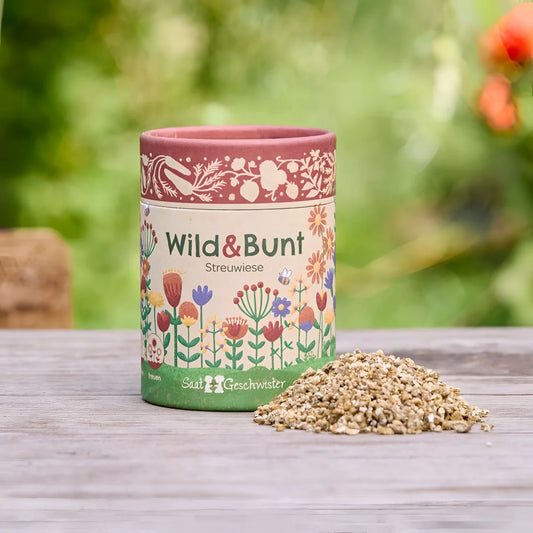 Ein zylindrischer terrakottabehälter mit einem bunten blumenetikett wild und bunt streuwiese und samenpellets daneben