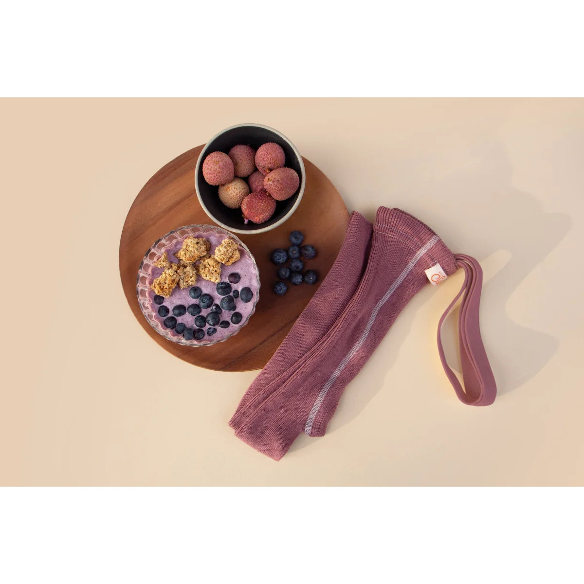 Runder Holztablett mit Obst und Smoothie neben lila Widerstandsband auf Strumpfhose