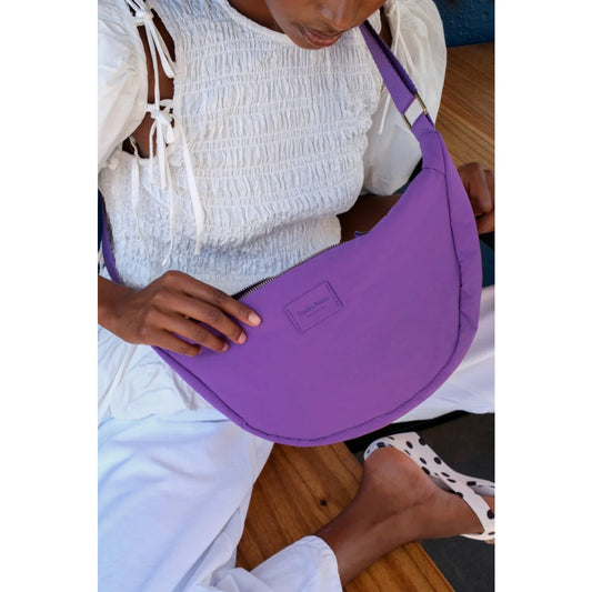 Texturierte gepolsterte erwachsenenbauchtasche aus violettem stoff mit geschwungenem design und markenpatch vorne