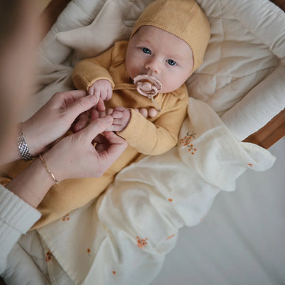 Baby in gelbem Overall und Hut auf floralem Musterdecke für 3er Pack Mulltuch