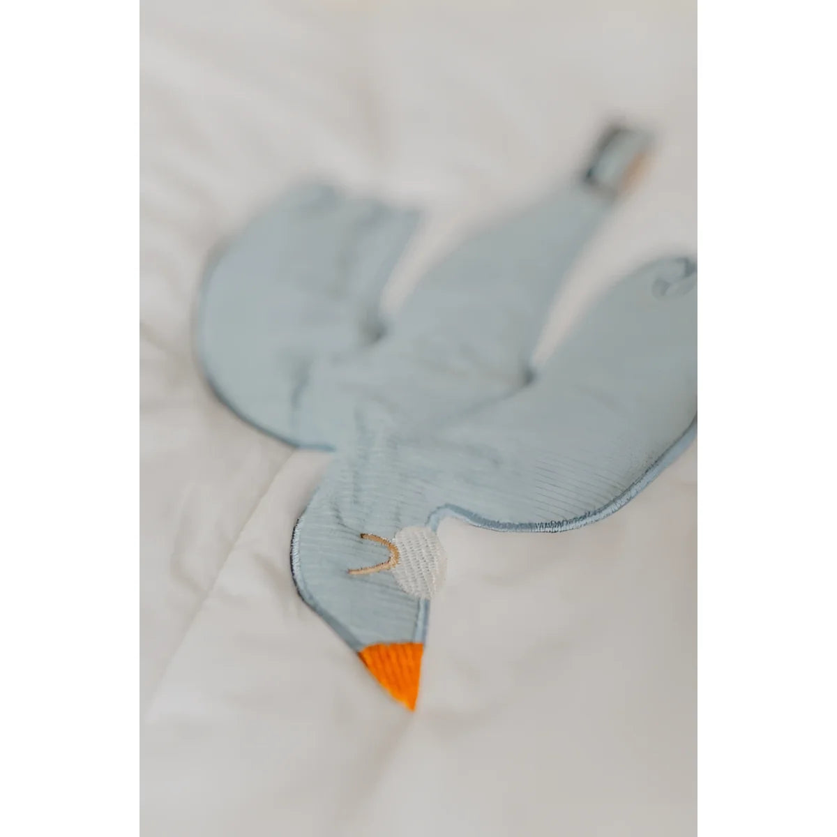 Ein soft hellblauer gestickter vogel-förmiger plüsch mit orangefarbenem schnabel auf einer activity decke für nachhaltige