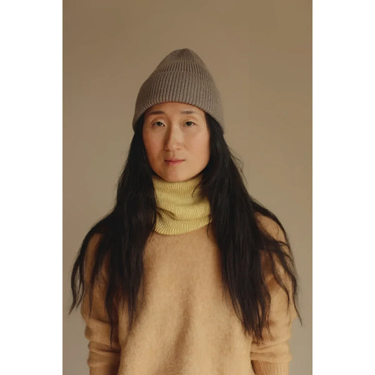 Frau mit langem dunklem Haar, Beanie, gelbem Rollkragen und beigem Pullover