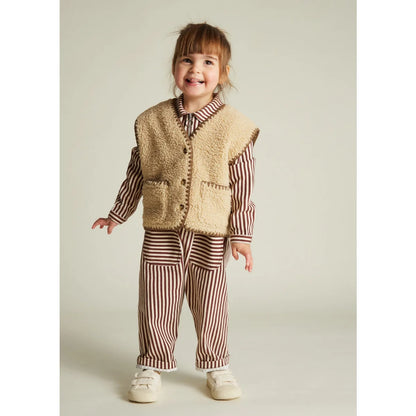 Beige Shearlingweste Amos Folk Gilet Sand mit braunen Knöpfen und Taschen über gestreiftem Hemd