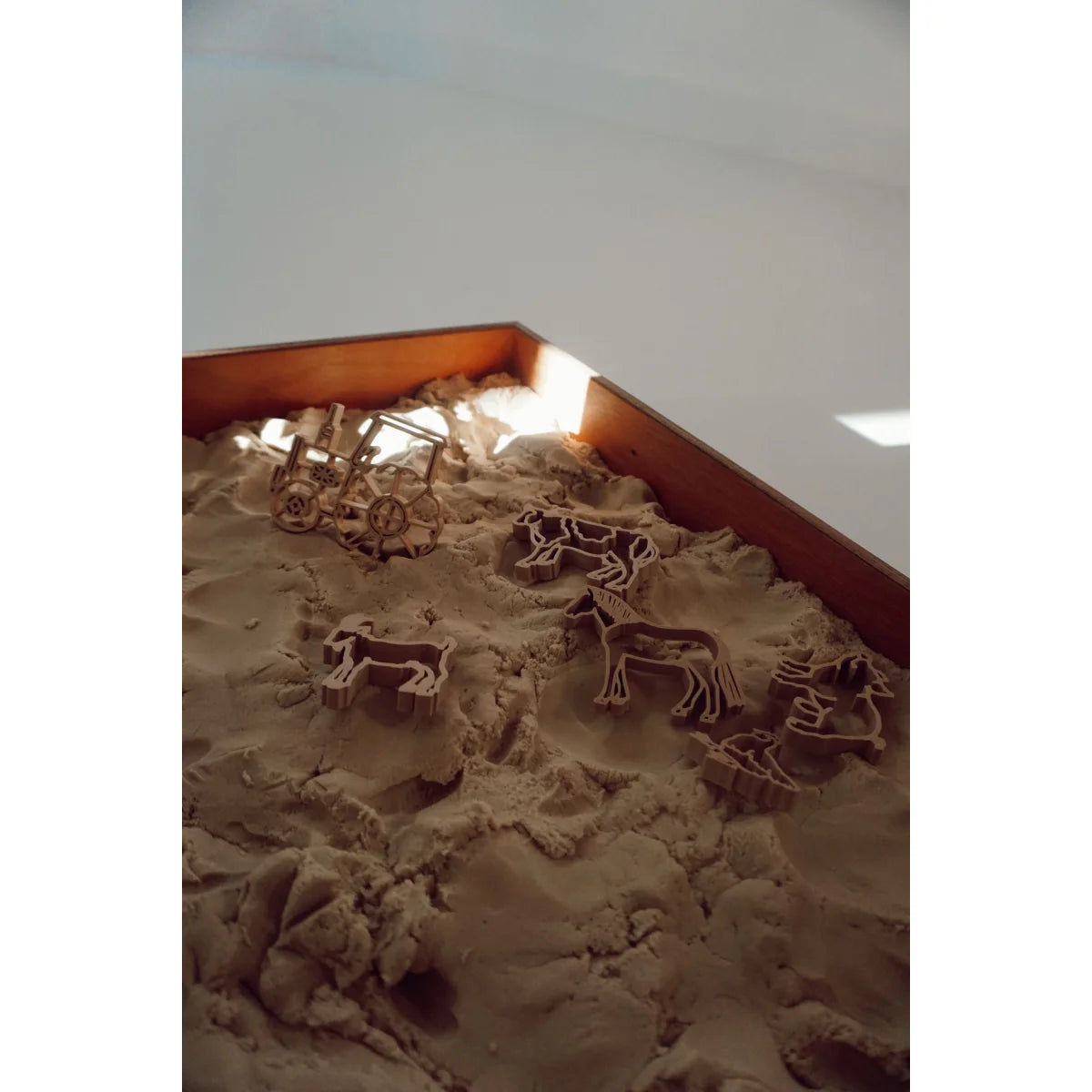 Tierförmige Ausstechformen und eine kleine Holzkarre im Sand für Kinderbacken