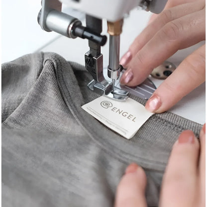 Sewing machine befestigt ein Etikett an grauem Stoff des Baby Body Langarm Walnuss