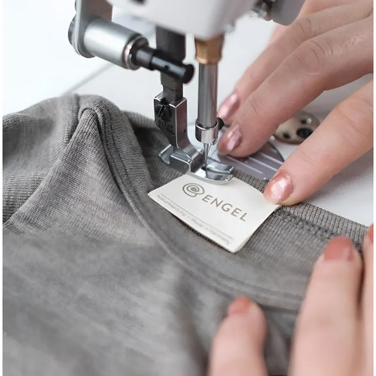 Sewing machine befestigt ein Etikett an grauem Stoff des Baby Body Langarm Walnuss