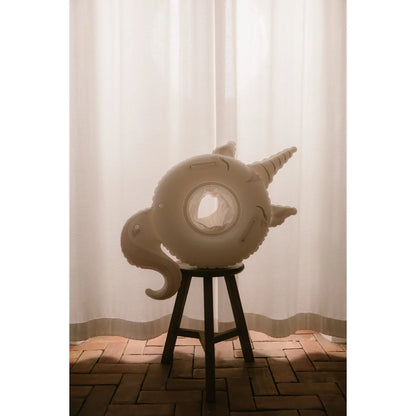 Baby-schwimmring sweet unicorn in off-white mit spirale horn und lockigem schwanz auf dunklem holzhocker für ökologische