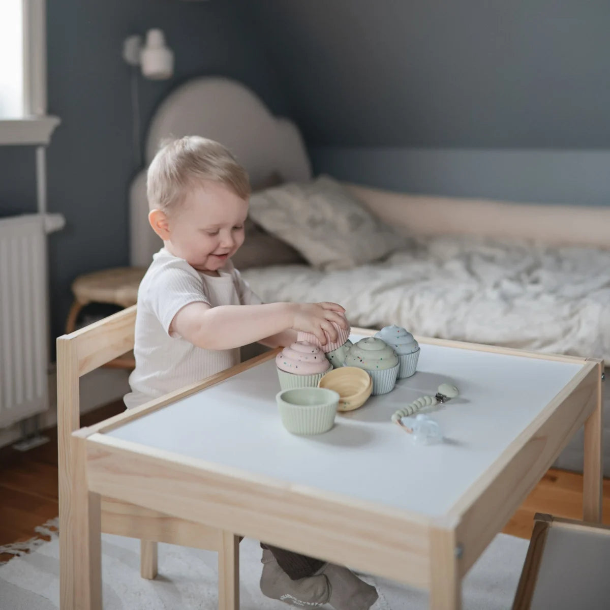 Junges Kind spielt mit bunten Holzspielzeugen am Tisch für Badespielzeug Cupcake