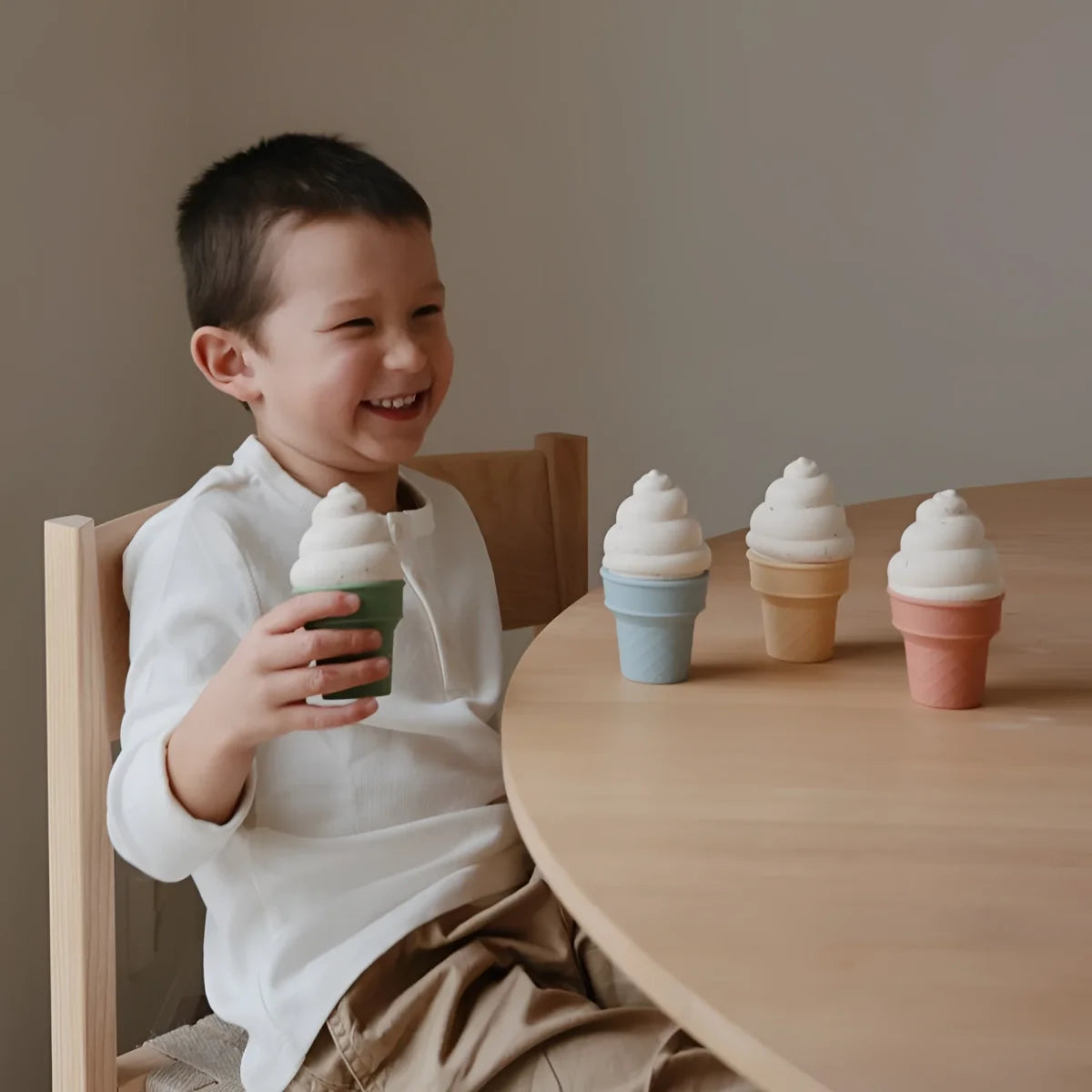 Ein kind hält einen grünen spielzeug-eisbecher aus holz mit weißer spiralcreme neben pastellfarbenen holzkegeln