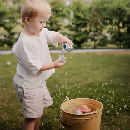 Ein kind gießt wasser mit einer hellblauen plastikgießkanne in einen gelben eimer mit schimmelresistentem badespielzeug space