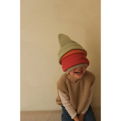 Jemand trägt gestapelte Wintermützen in Rot und Beige und lacht