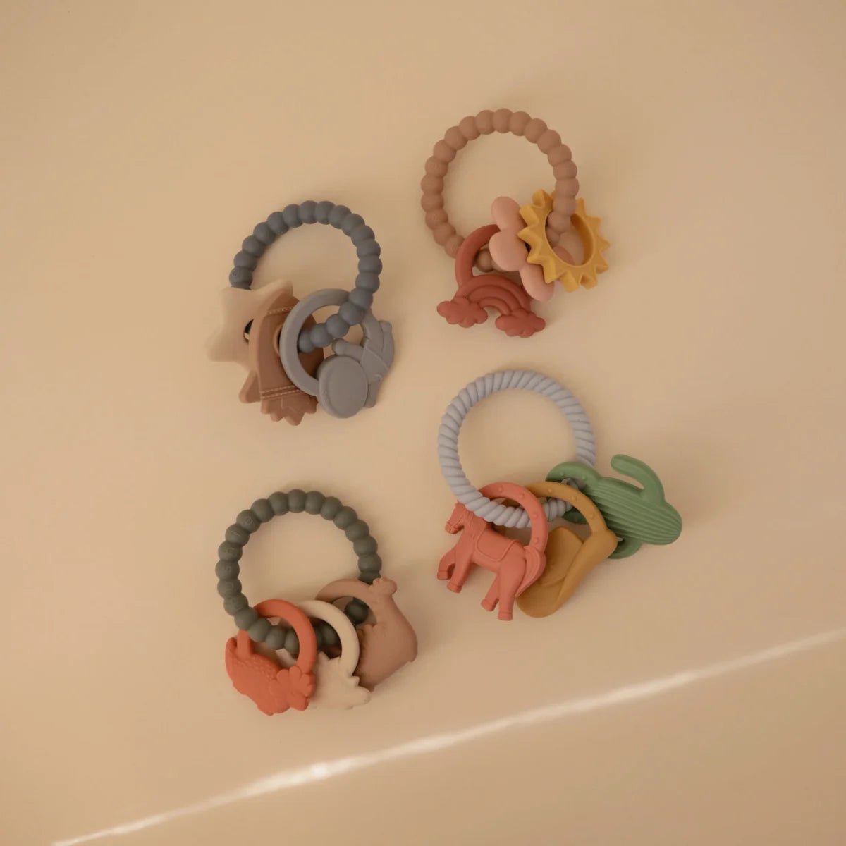 Vier pastellfarbene Silikon-Beißringe mit Dino- und Naturmotiven
