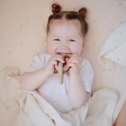 Lächelndes Baby mit zwei kleinen Haarsträußen in weißem Outfit und Beissring Kette