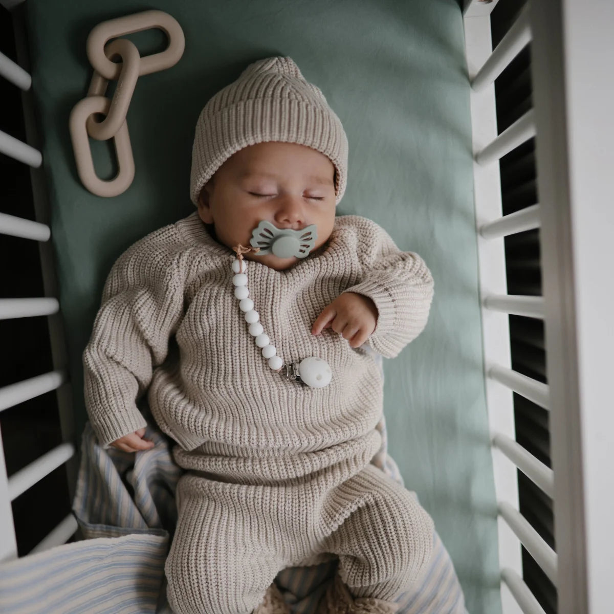 Schlafendes Baby in gestricktem Outfit und Hut mit Schnuller, Beissring Kette Shifting Sand