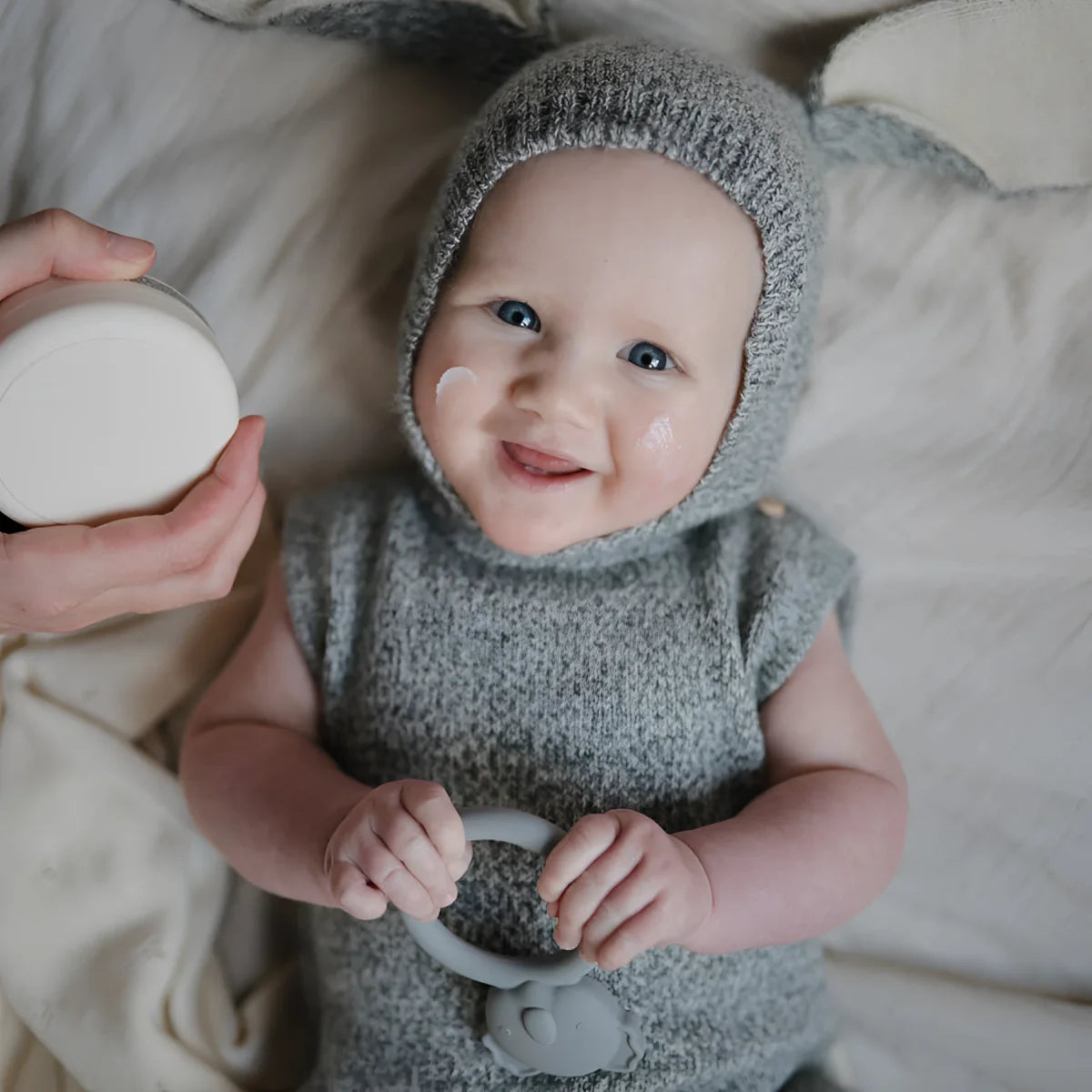 Lächelndes Baby in grauem Strickoutfit mit passender Mütze zum Beissring Koala