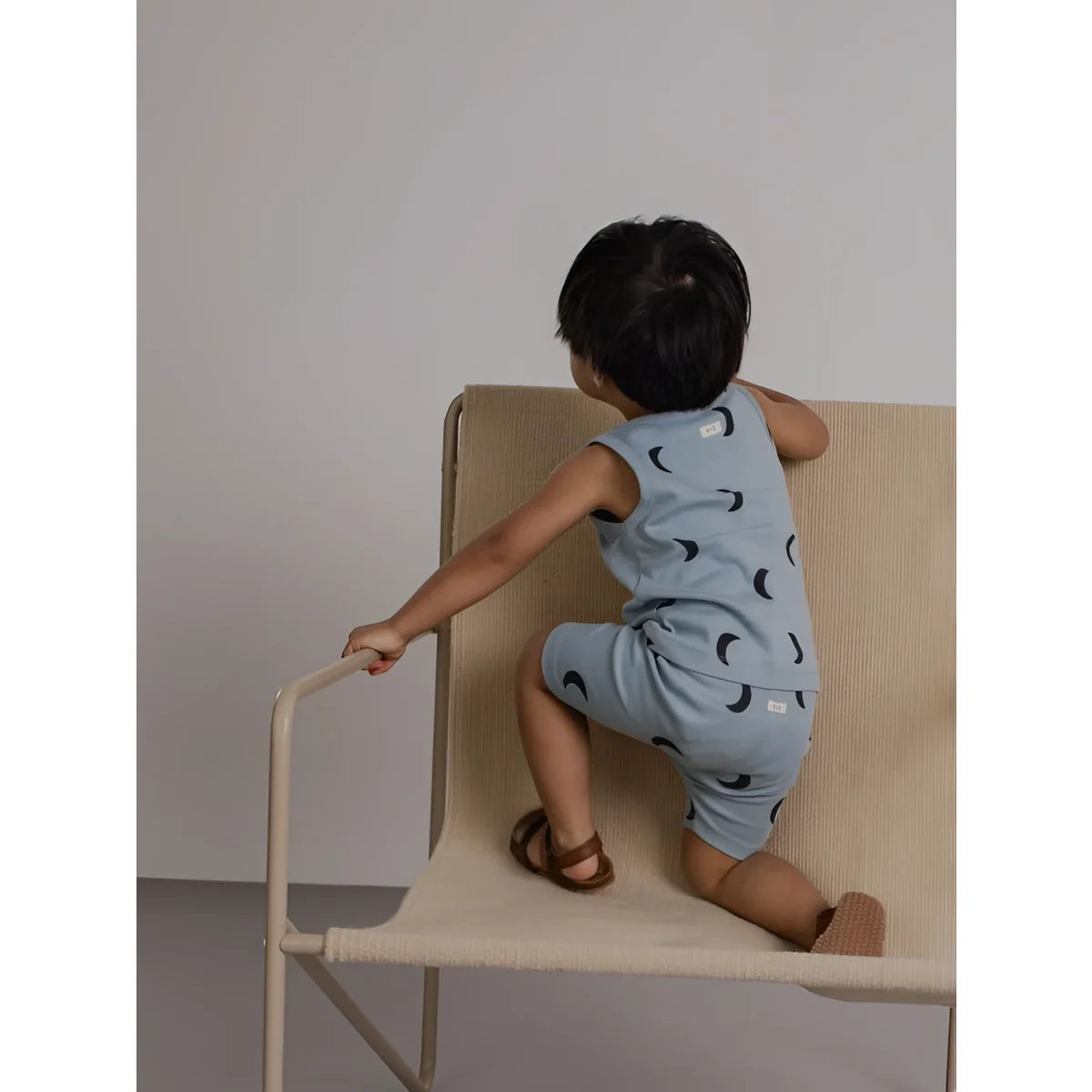 Kind in hellblauem Romper mit schwarzen Monden auf Beige-Sitzsack, River Midnight Biker Shorts