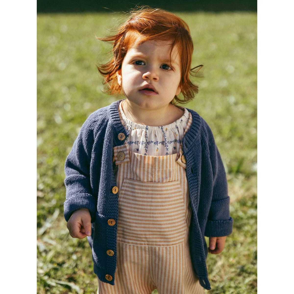 Nachhaltige Babykleidung Schweiz: Kind in gestricktem Cardigan über gestreiften Overalls
