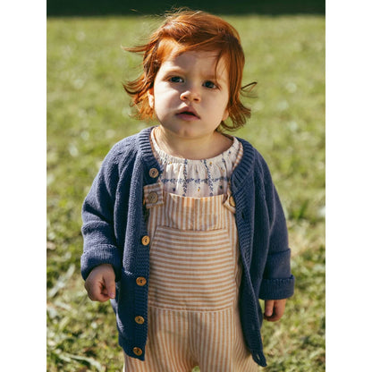 Nachhaltige Babykleidung Schweiz: Kind in gestricktem Cardigan über gestreiften Overalls