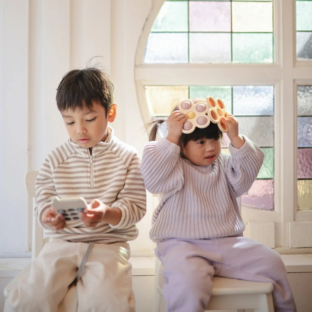 Zwei Kinder spielen mit Blume Plop-it Spielzeug in Lila und Gelb