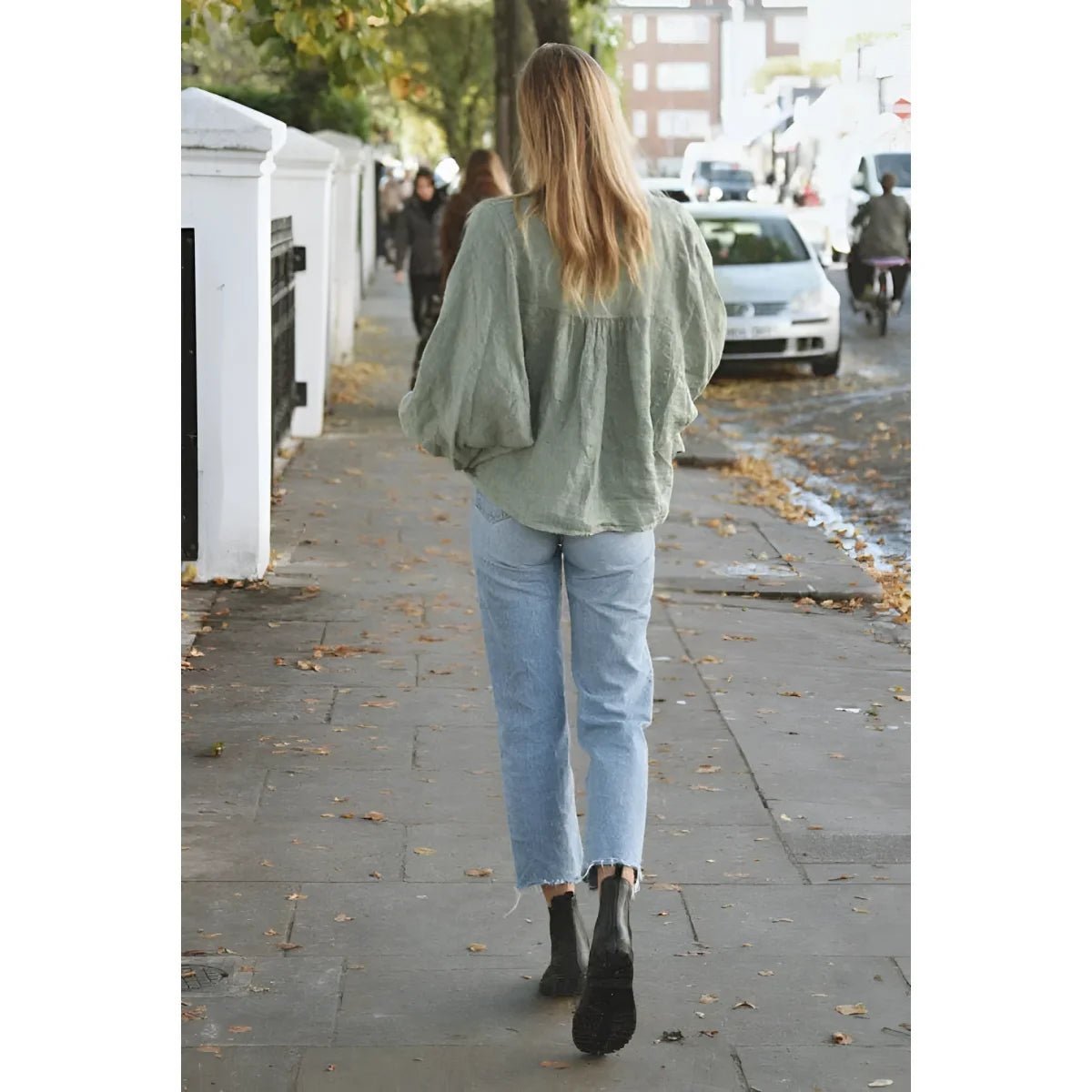 Person in einem salbeigrünen Sweater und hellblauen Jeans auf dem Bürgersteig