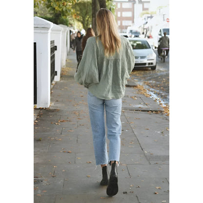 Person in einem salbeigrünen Sweater und hellblauen Jeans auf dem Bürgersteig