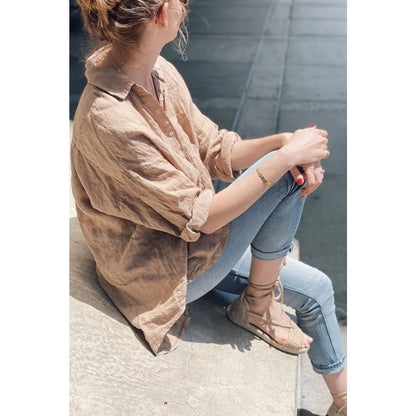 Frau trägt lockere beige Bluse und blaue Jeans, sitzt auf dem Boden