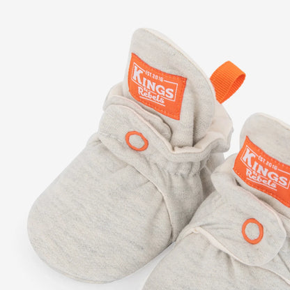 Graue strick-baby-booties aus baumwolle mit orangenem branding und zuglaschen nachhaltige babykleidung schweiz
