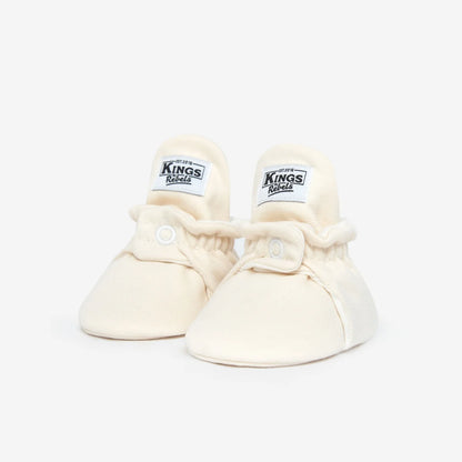 Ein Paar crèmefarbene Babybooties mit Kings-Labeln für 0-12 Monate
