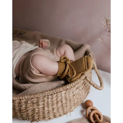 Neugeborenes Baby mit gestrickten Booties im gewebten Korb, Booties in Ocker