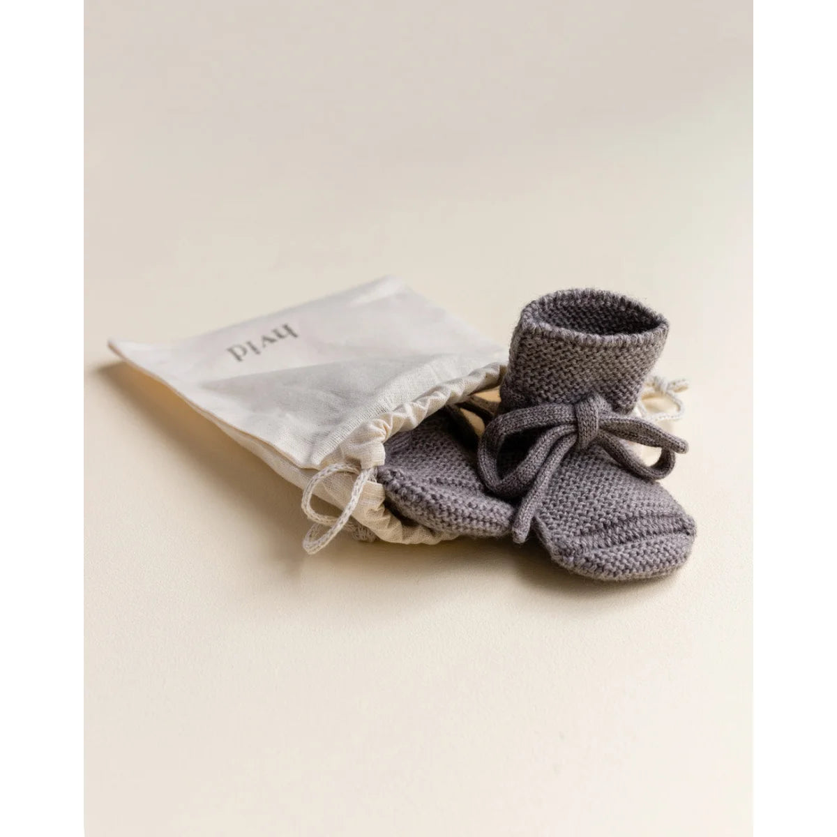 Grau gestrickte Babybooties mit Schleifen, begleitet von einem kleinen Stoffbeutel